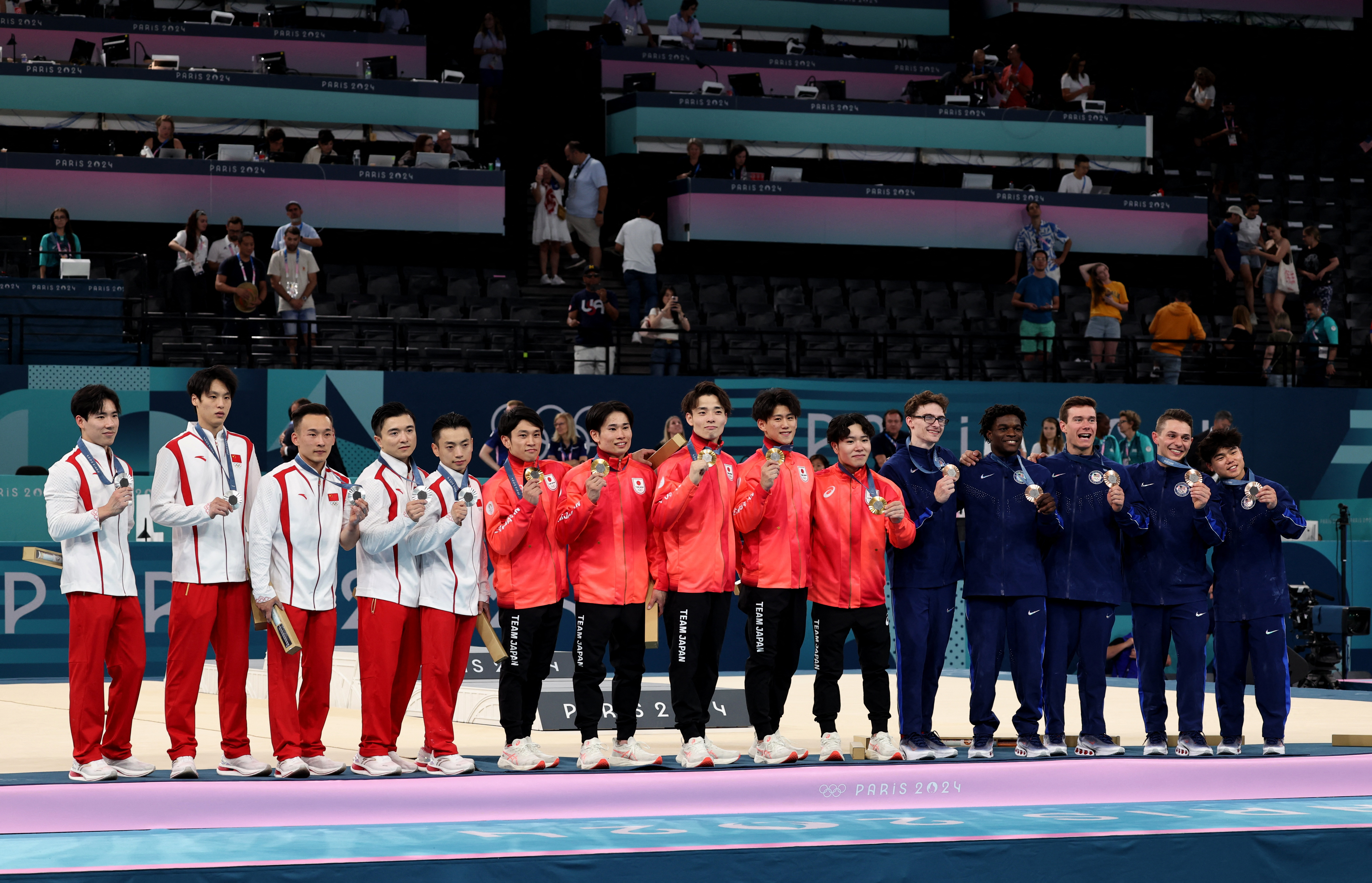Men's Artistic Gymnastics - Paris 2024 Olympic - Men's Team Victory Ceremony - Bercy Arena, Paris, France - July 29, 2024. Gold medalists Daiki Hashimoto, Kazuma Kaya, Shinnosuke Oka, Takaaki Sugino and Wataru Tanigawa of Japan celebrate on the podium with silver medallist's Weide Su, Jingyuan Zou, Boheng Zhang, Ruoteng Xiao and Yang Liu of China and bronze medallist's Stephen Nedoroscik, Paul Juda, Brody Malone, Frederick Richard and Asher Hong of United States REUTERS/Mike Blake